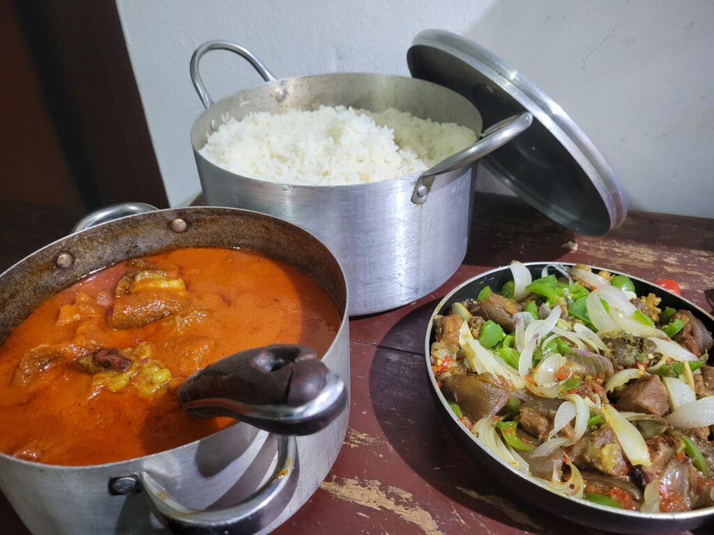 a small kitchen table containing a pot of stew, a pot of rice and saucepan of asun 